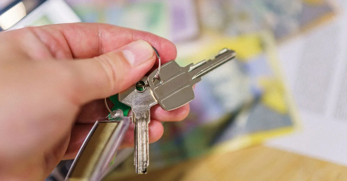 Gros plan sur des clés dans une main représentant la propriété immobilière avec des documents financiers flous en arrière-plan.